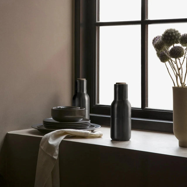 Audo Copenhagen Bottle Grinder Large Set Ash Carbon auf Fensterbank mit dunklem Geschirr
