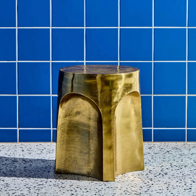 House Doctor Riga Beistelltisch Antikgold als Hocker vor blauer Fliesenwand