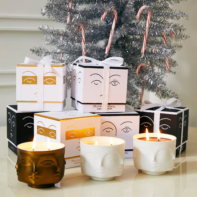 Jonathan Adler Muse Duftkerzen Kollektion – Muse Noir, Muse Blanc und Muse Or brennend vor Weihnachtsbaum mit Geschenkboxen