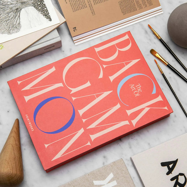 Art of Backgammon von Printworks – Verpackung dekorativ zwischen Kunstbüchern und Pinseln platziert