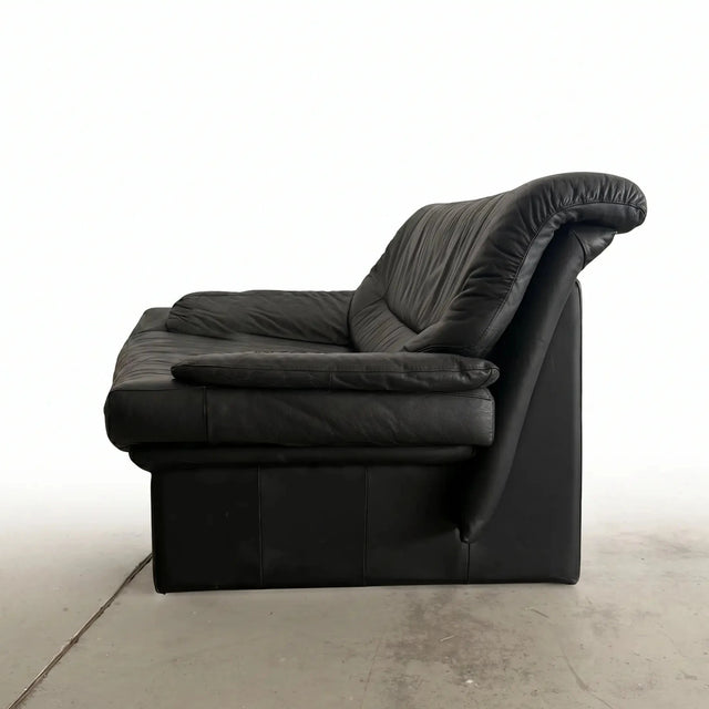 Seitenprofil eines postmodernen Design-Sofas aus schwarzem Leder mit weich fallender Kissen-Armlehne auf weißem Hintergrund